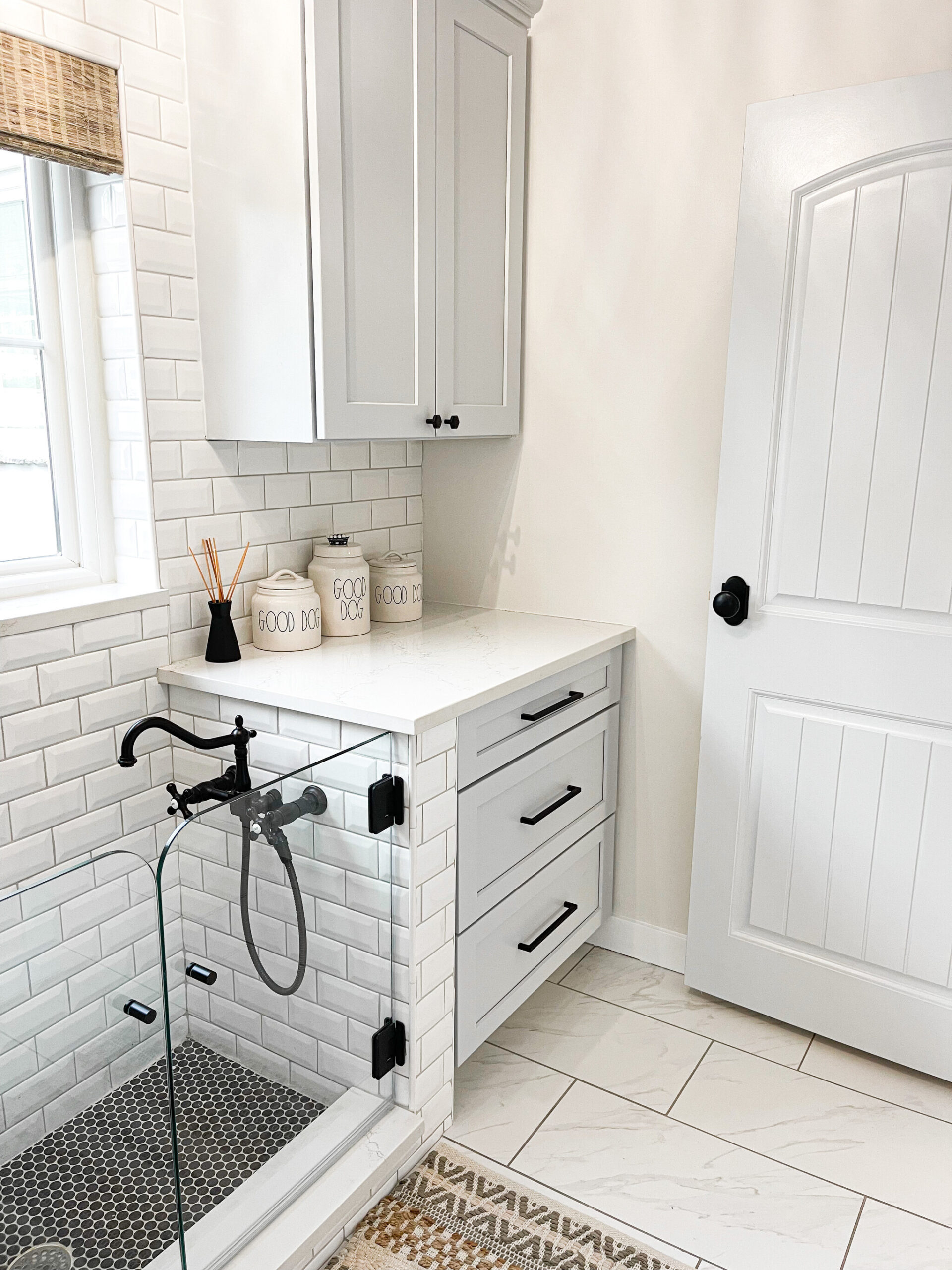 Modern mud room with black hardware, white tile, and a dog washing station